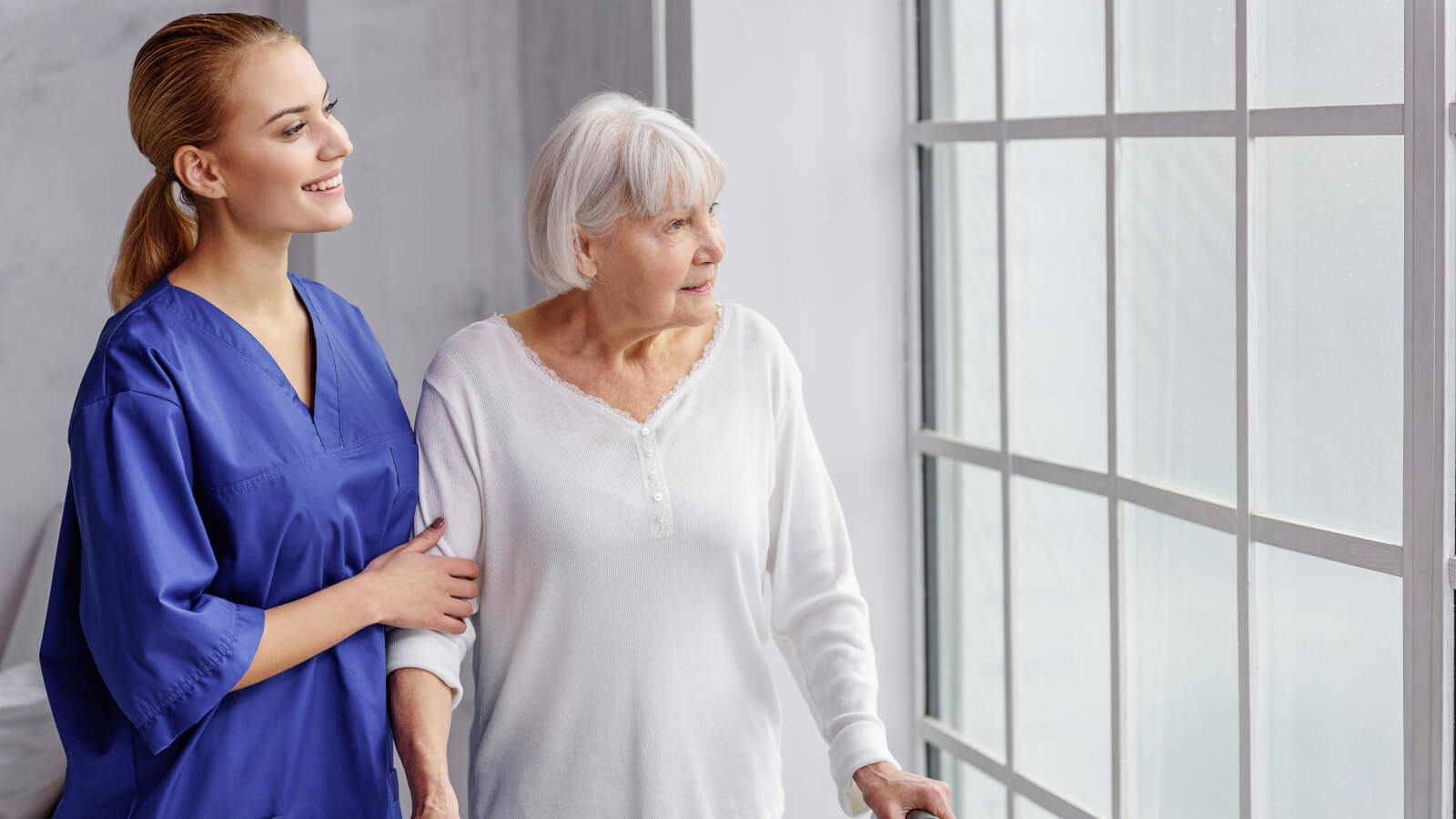 Nurse looking out the window with her elderly patient.